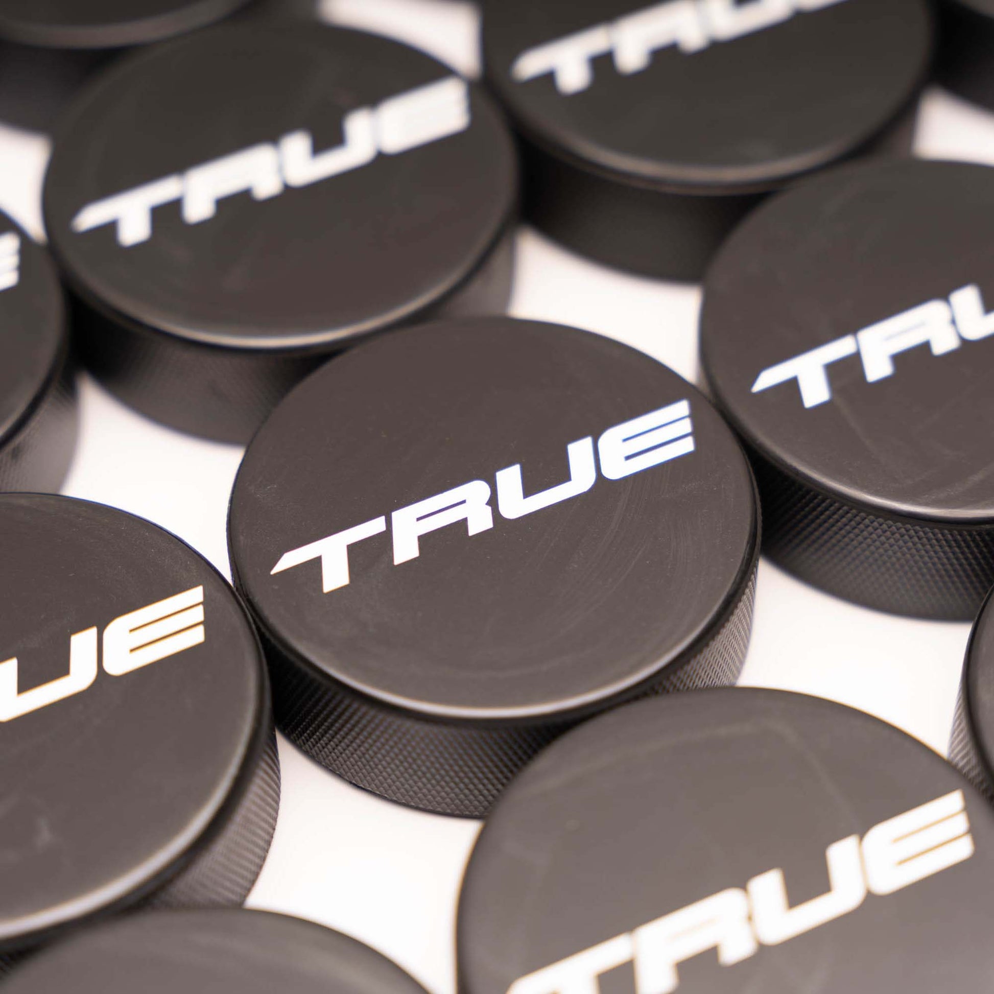 Multiple black hockey pucks with 'TRUE' branding in white