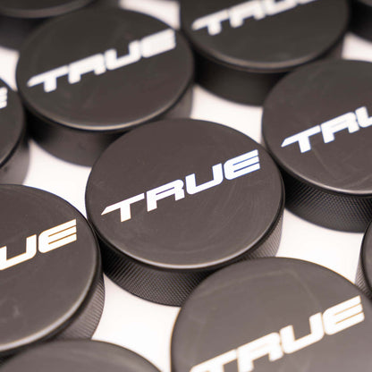 Multiple black hockey pucks with 'TRUE' branding in white