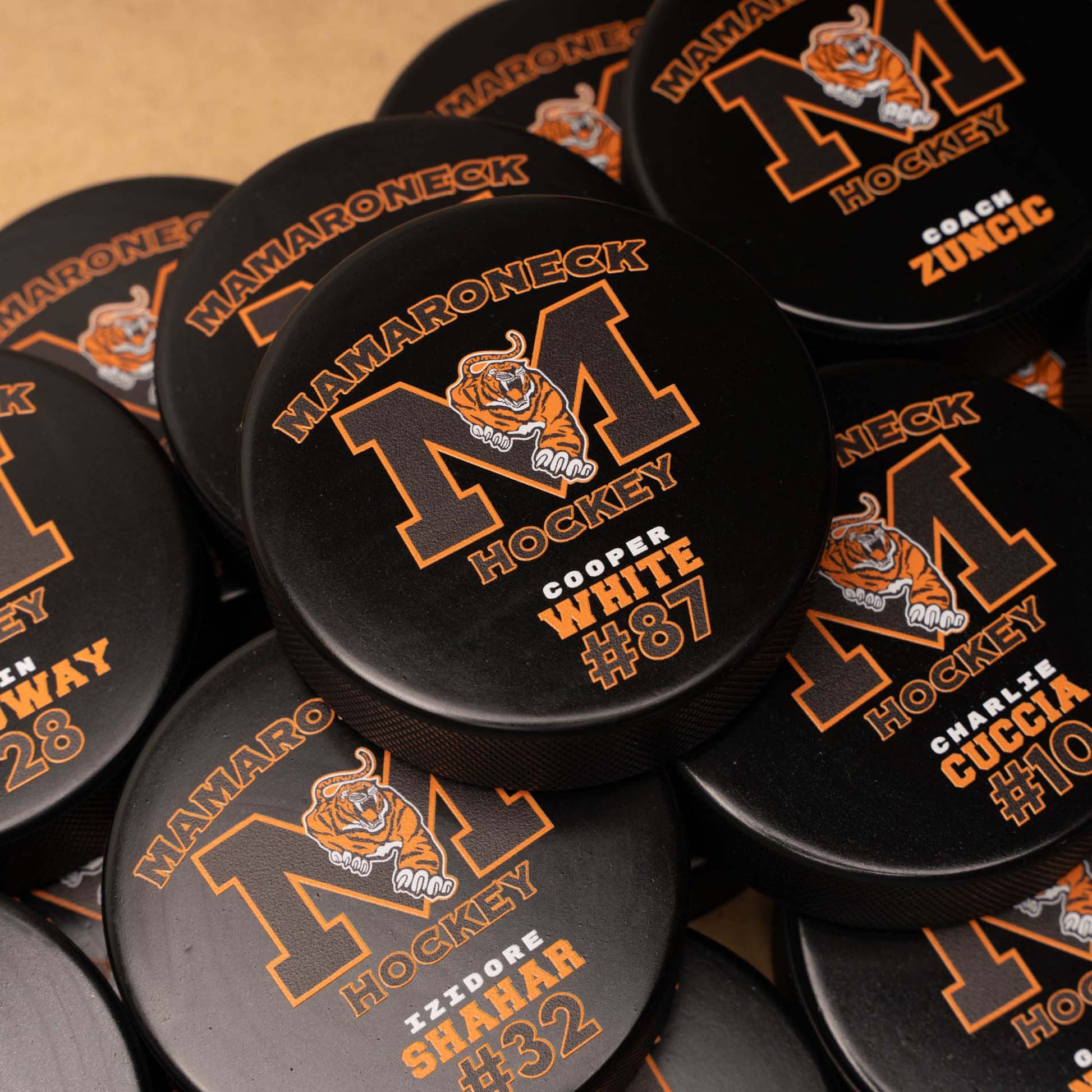 Collection of Mamaroneck Hockey pucks with personalized names and numbers.
